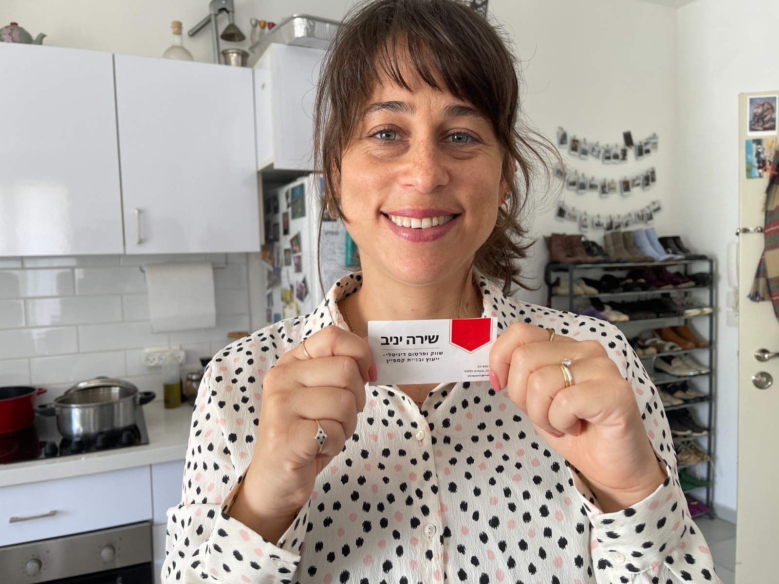 שירה מחייכת ומציגה למצלמה את כרטיס הביקור שלה.