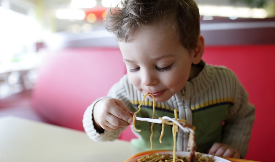 תמונה של ילד יושב ליד שולחן ואוכל ספגטי